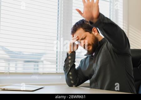 Erschöpfter denkender Manager, der im Büro mit Dokumenten arbeitet, geschlossener Laptop auf dem Schreibtisch. Stockfoto