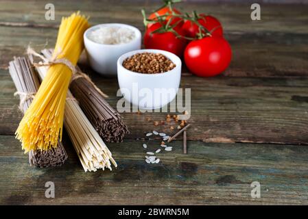 Bündel der Italienische Spaghetti, raw Soba Nudeln und comen, Schüsseln mit Buchweizen und Reis mit Tomate auf einem alten hölzernen Hintergrund, flay legen mit Kopie spac Stockfoto