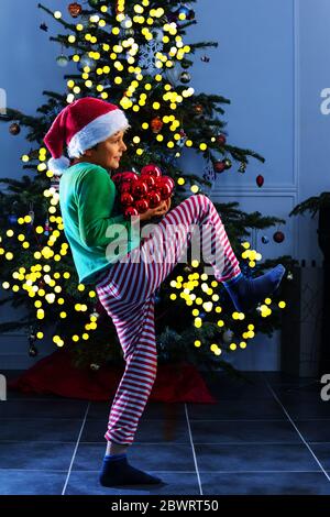 Kind Junge schleichen und schmücken Weihnachtsbaum sitzen in festlichen Kostüm der Elfe am Abend Stockfoto