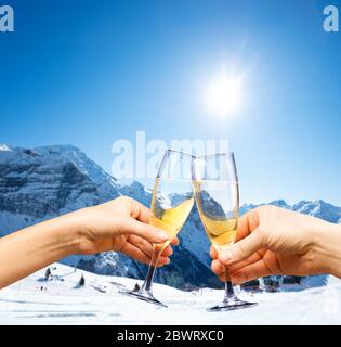 Zwei Hände halten Gläser Champagner über dem Skigebiet und Range auf das gute sonnige Wetter Stockfoto