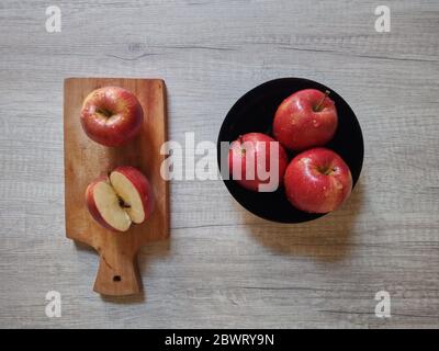 Frische rote Äpfel mit Wassertropfen auf einem hölzernen Hintergrund mit geschnittenen Äpfeln isoliert. Gesundes Lifestyle-Fotokonzept. Indonesien Stockfoto