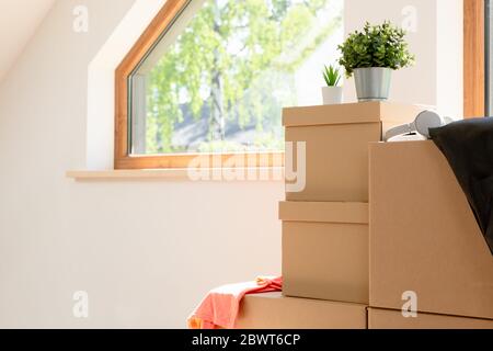 Verschieben. Pappkartons für den Umzug in ein neues, sauberes Zuhause. An einem sonnigen Tag durch ein Fenster im Dachgeschoss. Stockfoto