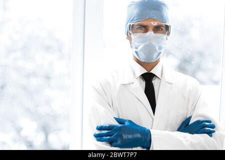 Schließen Sie up.serious Arzt in einer Schutzmaske in der Nähe des Fensters. Stockfoto