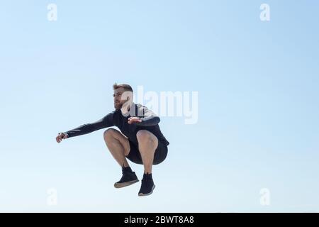 Porträt eines jungen bärtigen Athleten von 25 Jahren, der gegen einen blauen Himmel Athleten springt, der entlang der Küste läuft, Draufsicht. Aktiver Lebensstil. Junger Mann Stockfoto