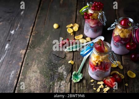 Glas mit hausgemachtem Müsli und Joghurt mit Chia, Erdbeeren und Brombeeren auf Holzbrett Stockfoto