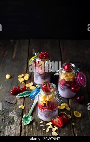 Glas mit hausgemachtem Müsli und Joghurt mit Chia, Erdbeeren und Brombeeren auf Holzbrett Stockfoto