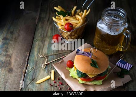 Hausgemachter Burger mit Brötchen und us-Flagge, Rindfleisch mit einem Glas dunklem Bier und Pommes frites auf Holzboden. Unabhängigkeitstag Stockfoto