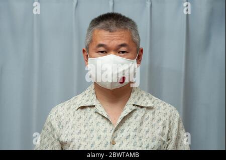 COVID-19 Pandemic - Vorderansicht Porträt des mittleren Alters asiatischen Mann trägt DIY hausgemachte chirurgische Gesichtsmaske mit Japan-Flagge. Schutz vor Coronavirus. Stockfoto