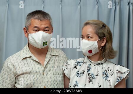 COVID-19 Pandemic - Vorderansicht Porträt des mittleren Alters Paar trägt DIY hausgemachte chirurgische Gesichtsmaske mit Brasilien und Japan Flagge. Stockfoto