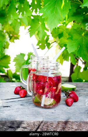 Erdbeer-Limonade mit Kalk im Einmachglas auf einem Holztisch vor dem Hintergrund der Weinreben Stockfoto