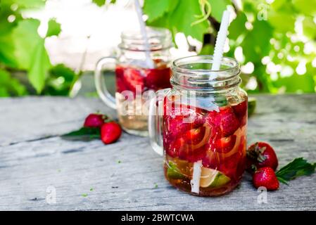 Frische rote Erdbeerlimonade im Einmachglas auf einem Holztisch vor dem Hintergrund von Weinreben. Sommergetränke und Cocktails Stockfoto