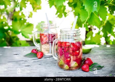 Erdbeer-Limonade mit Kalk im Einmachglas auf einem Holztisch vor dem Hintergrund der Weinreben Stockfoto
