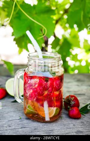 Frische rote Erdbeerlimonade im Einmachglas auf einem Holztisch vor dem Hintergrund von Weinreben. Sommergetränke und Cocktails Stockfoto