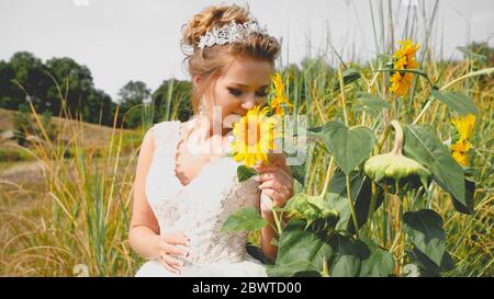 Getöntes Porträt von eleganten jungen Braut riechenden Sonnenblume auf dem Feld Stockfoto