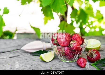Zutaten für Erdbeer Mojito auf einem Holztisch vor dem Hintergrund von Weinreben. Sommergetränke und Cocktails Stockfoto