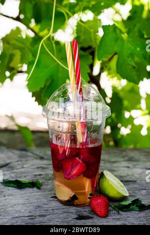 Frische rote Erdbeerlimonade auf einem Holztisch vor dem Hintergrund von Weinreben. Sommergetränke und Cocktails Stockfoto
