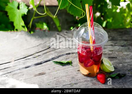 Frische rote Erdbeerlimonade auf einem Holztisch vor dem Hintergrund von Weinreben. Sommergetränke und Cocktails Stockfoto