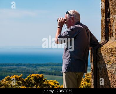 Senior Mann schaut durch Fernglas an sonnigen Tag in Sicht, East Lothian, Schottland, Großbritannien Stockfoto