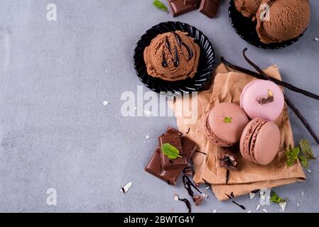Schokoladen-Makronen mit Eis, Stücke von schwarzer Schokolade, Vanille-Stick und Minze auf einem Stein Hintergrund, lag flach Stockfoto