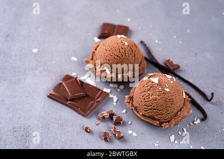 Zwei Kugeln Schokoladeneis mit einem Vanille-Stick und Stücke von Schokolade auf einem dunklen Hintergrund Stockfoto