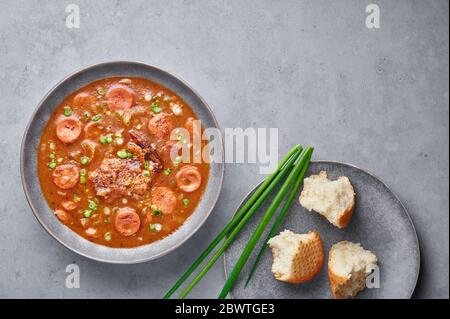 Hähnchen und Wurst Gumbo Suppe in grauen Schüssel auf Beton Hintergrund. Gumbo ist louisiana cajun Cuisine Suppe mit Roux. Amerikanische Küche in den USA. Traditionelle Ethnische Stockfoto