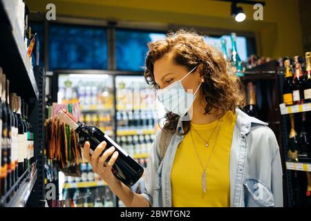Junge Frau mit Schutzmaske wählt Wein im Supermarkt. Stockfoto
