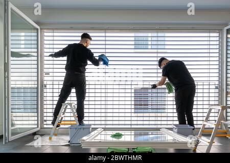 Horizontale Ansicht von zwei männlichen professionellen Reinigern Reinigung Jalousien auf einer großen Fensterfront mit Mikrofasertüchern Stockfoto