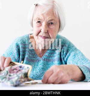 Betroffene ältere Frau am Tisch sitzen zählen Geld in Ihrem Portemonnaie. Stockfoto