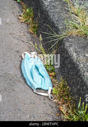 Nahaufnahme einer ausrangierten medizinischen Gesichtsmaske, die in der Rinne einer britischen Wohnstraße isoliert ist. Gefährliche Abfälle auf der Straße. Stockfoto