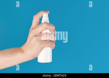 Hand hält eine weiße Sprühflasche, isoliert vor blauem Hintergrund Stockfoto