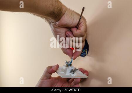 Die Hände eines Mannes lösen elektrische Kabel von einem alten Lichtschalter Stockfoto