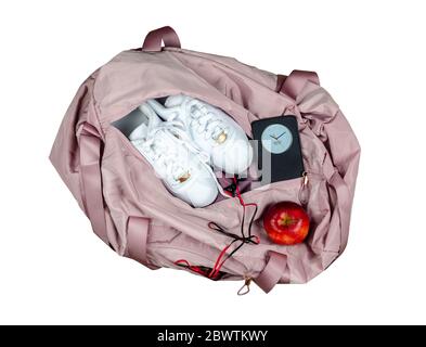 Damen rosa Turnbeutel mit weißen Turnschuhen, roten Apfel und Smartphone zeigt Zeit und Datum, isoliert auf weißem Hintergrund Stockfoto