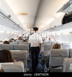 Innenraum eines kommerziellen Flugzeugs mit Flugattachant, der Passagiere während des Fluges auf den Sitzen bedient. Steward in Uniform, der den Gang geht.Square Stockfoto
