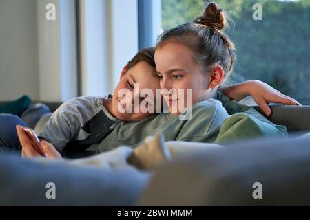 Bruder und Schwester sitzen zu Hause auf der Couch mit dem Smartphone Stockfoto