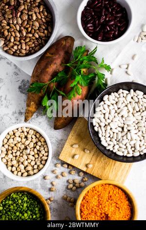 Süßkartoffeln, Petersilie und Schalen mit verschiedenen Bohnen und Linsen Stockfoto