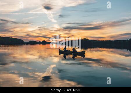 Junge Leute, die bei Sonnenuntergang auf dem See Boot fahren Stockfoto