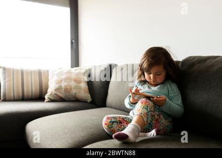 Kleinkind Mädchen sitzt auf der Couch zu Hause mit Smartphone Stockfoto