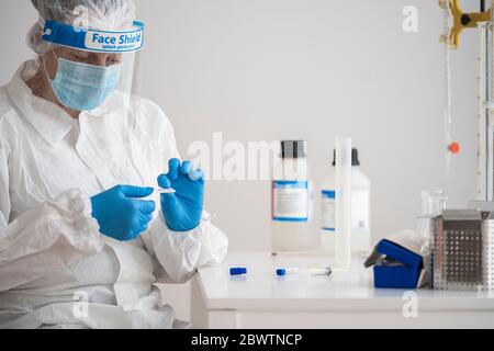 Frau in Schutzkleidung sitzt am Schreibtisch Forschung über Epidemiologie Stockfoto