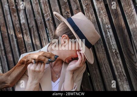 Lachende Frau mit Hut, der die Pfote ihres Hundes hält Stockfoto