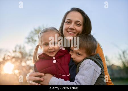 Portrait von glücklicher Mutter umarmt zwei Kinder im Freien Stockfoto