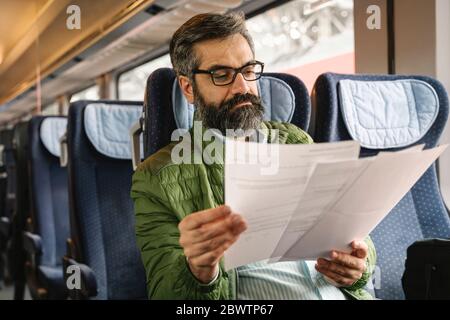 Mann, der im Zug sitzt und Dokumente liest Stockfoto