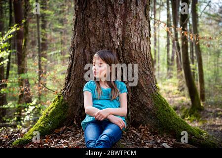 Portrait von Mädchen mit geschlossenen Augen lehnt sich an Baumstamm im Wald Stockfoto