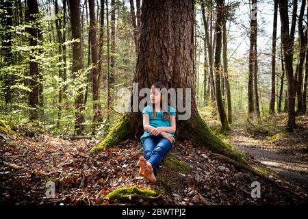 Mädchen mit geschlossenen Augen lehnt sich an Baumstamm im Wald Stockfoto