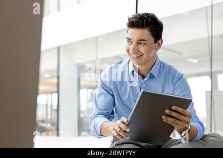 Porträt eines lächelnden jungen Geschäftsmannes mit Tablet am Fenster im Büro Stockfoto