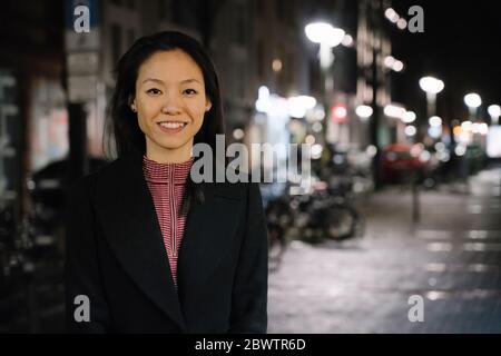 Porträt einer selbstbewussten jungen Frau in der Stadt bei Nacht, Frankfurt, Deutschland Stockfoto