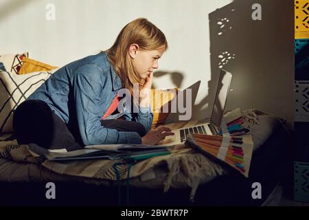 Mädchen sitzt auf dem Bett zu Hause Hausaufgaben zu tun und mit Laptop Stockfoto