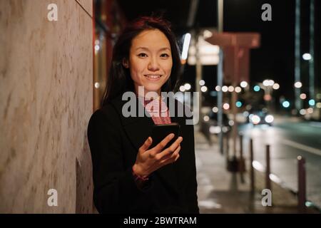 Porträt einer jungen Frau mit Smartphone in der Stadt bei Nacht, Frankfurt, Deutschland Stockfoto
