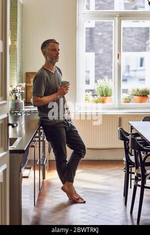 Reifer Mann hält Tasse in der Küche zu Hause Stockfoto