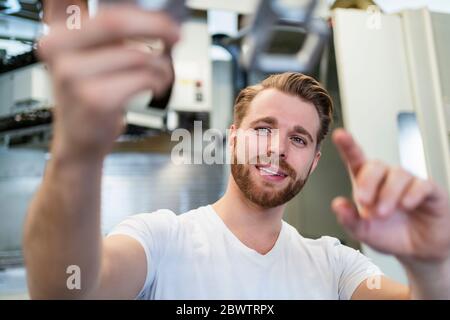 Lächelnder junger Mann, der ein Werkstück in einer Fabrik hält Stockfoto