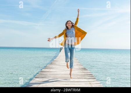 Glückliche Frau, die Musik mit Kopfhörern auf dem Steg, Mallorca, Spanien hört Stockfoto